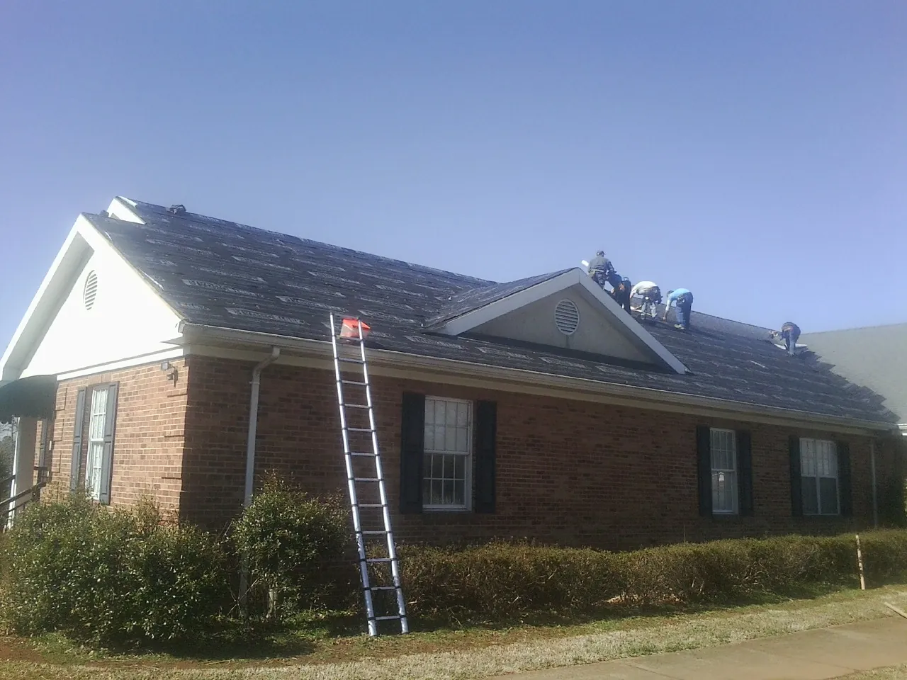 Crew tearing shingles off a brick ranch roof with a ladder set — Metal Roof Repair work by our crew in Rushville
