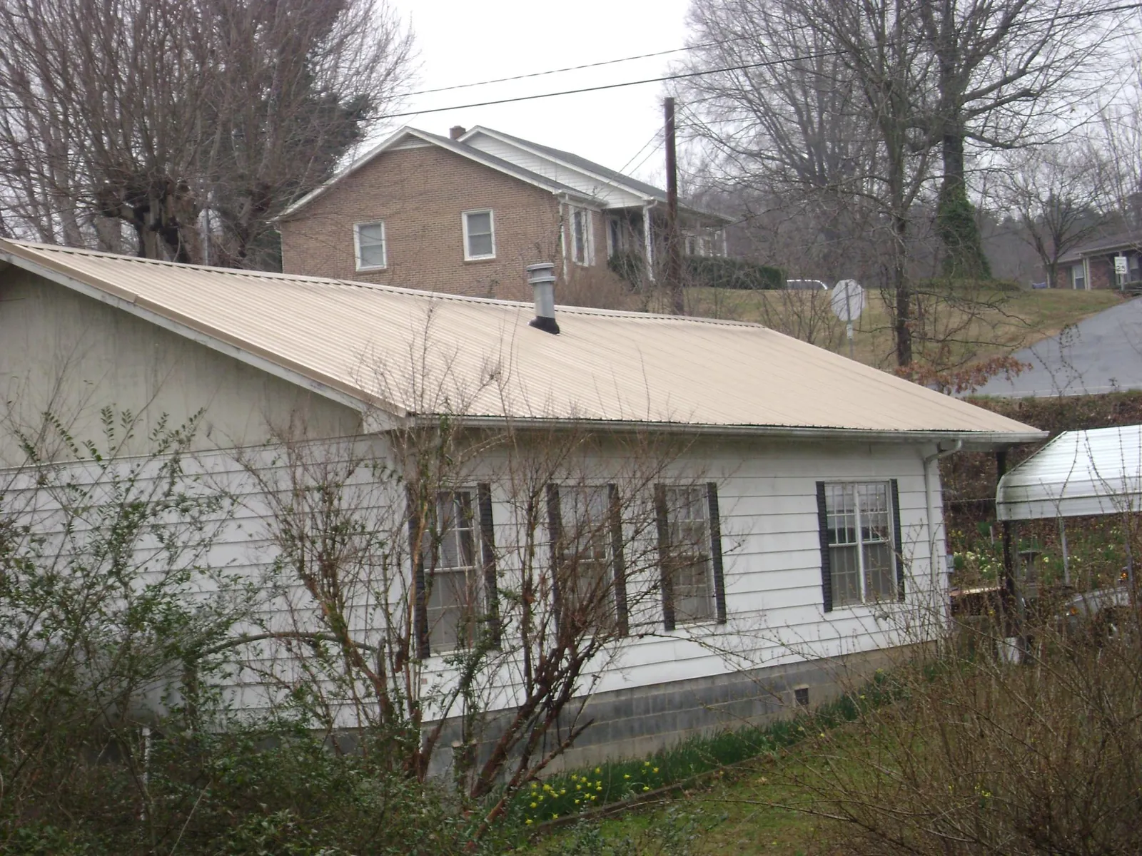 Tan metal roof on a white sided house set into a hillside — Commercial Roofing by Roofing Brothers in Rushville